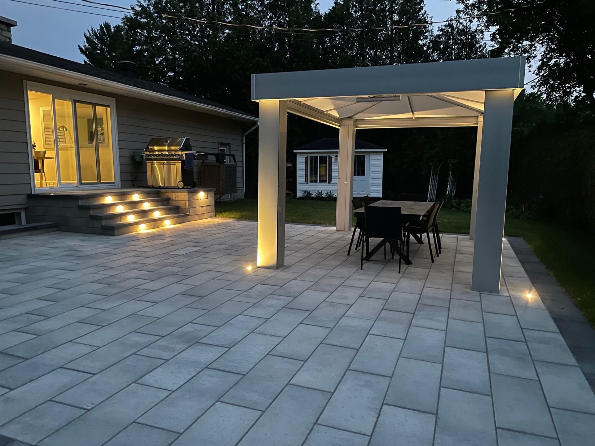 Un patio avec une table et des chaises sous une pergola la nuit.