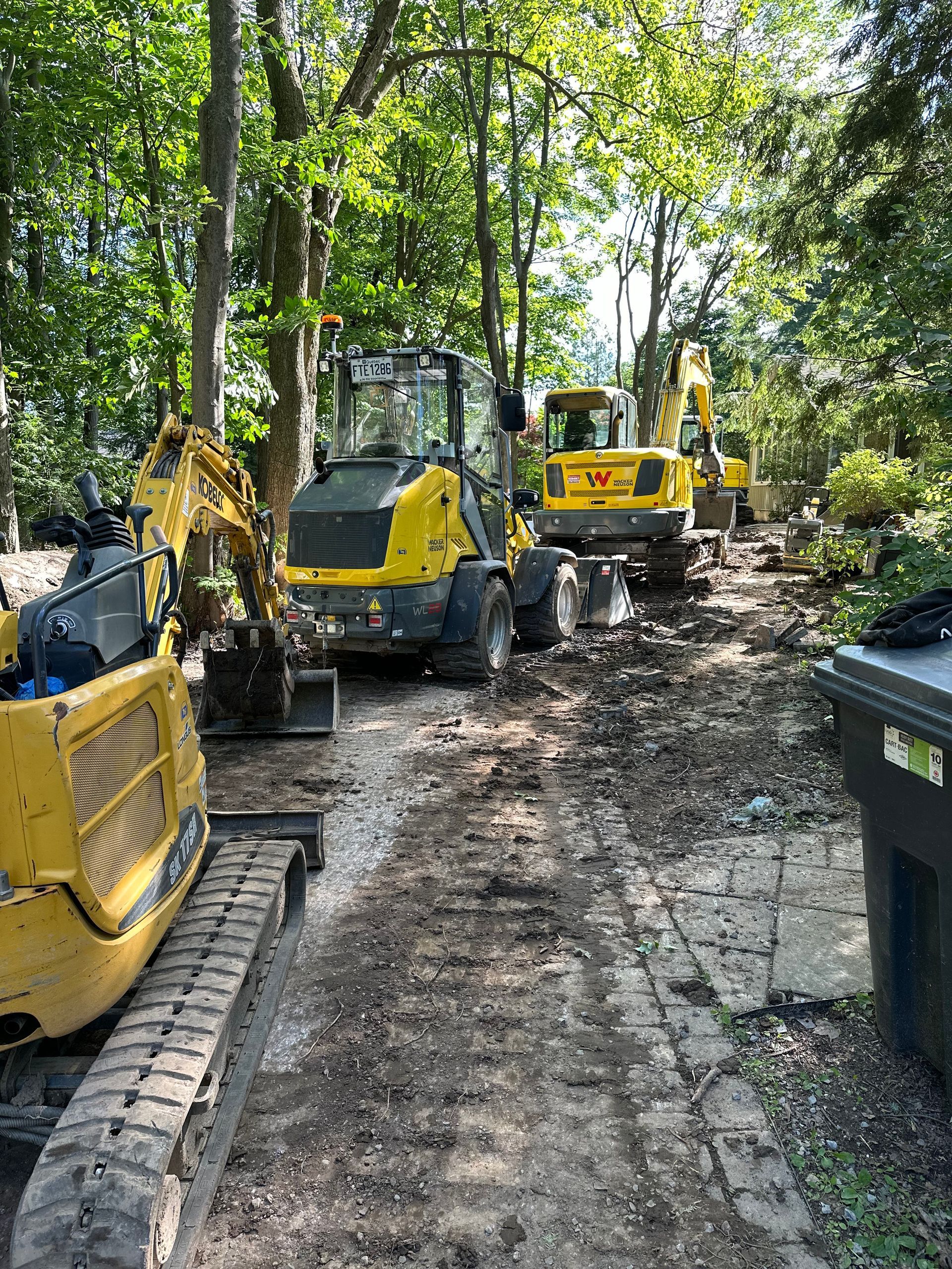 Un groupe de véhicules de construction est garé sur un chemin de terre dans les bois.