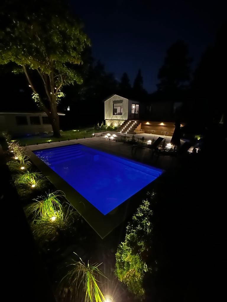 Une grande piscine est éclairée la nuit dans une cour arrière.
