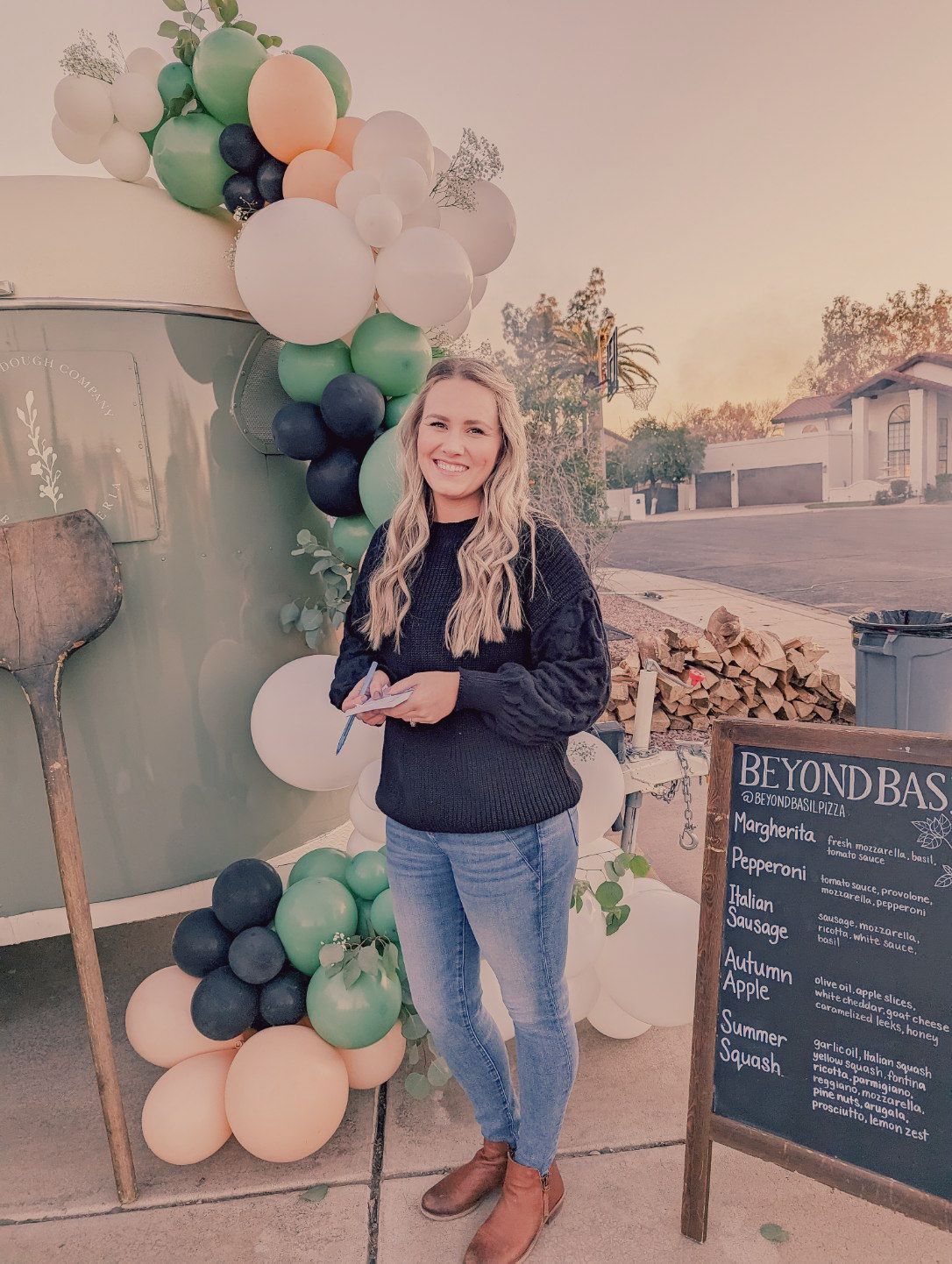 A woman is standing behind Beyond Basil Mobile Pizzeria serving food.
