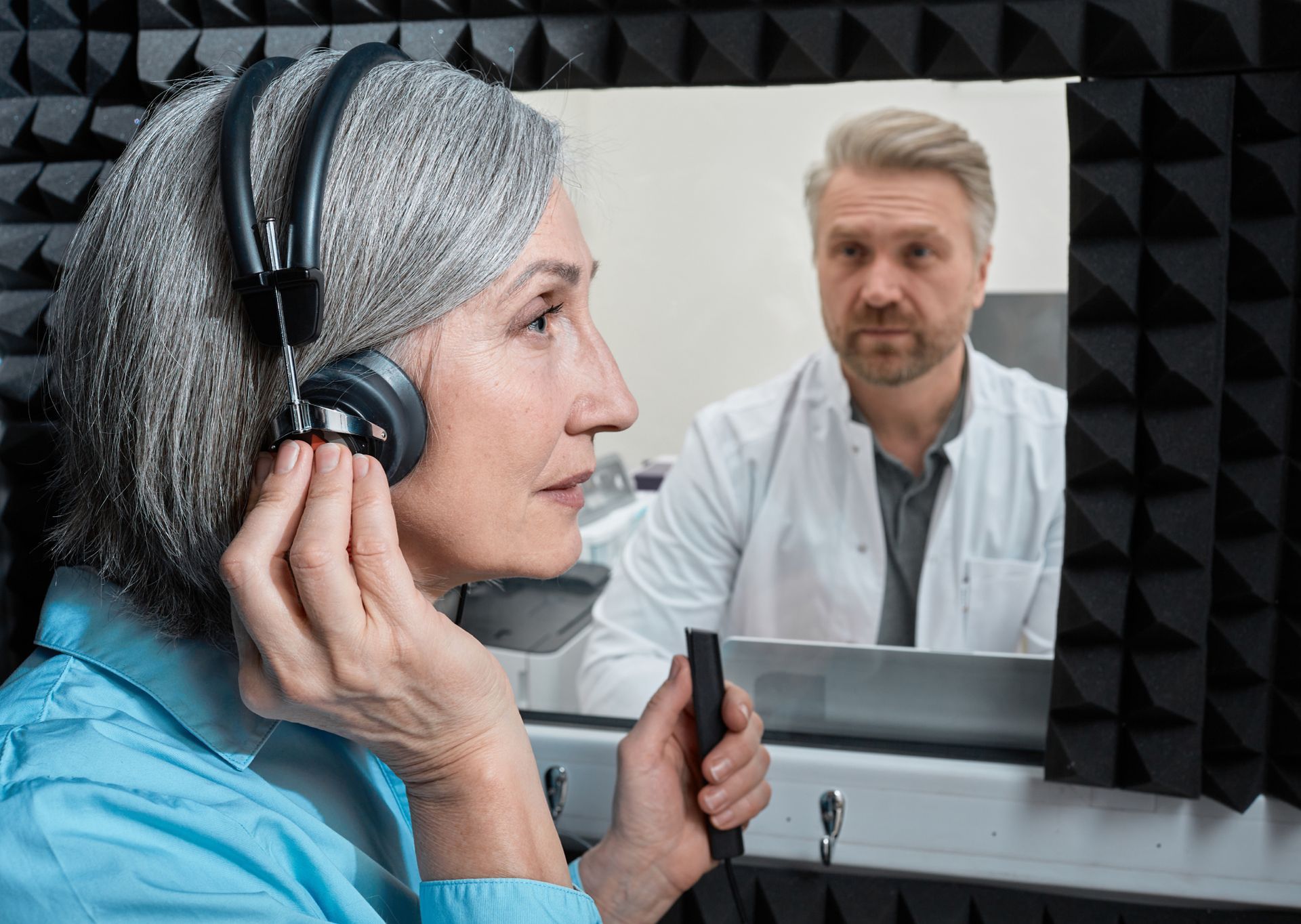 Woman undergoing comprehensive hearing test with audiologist in soundproof booth wearing headphones.