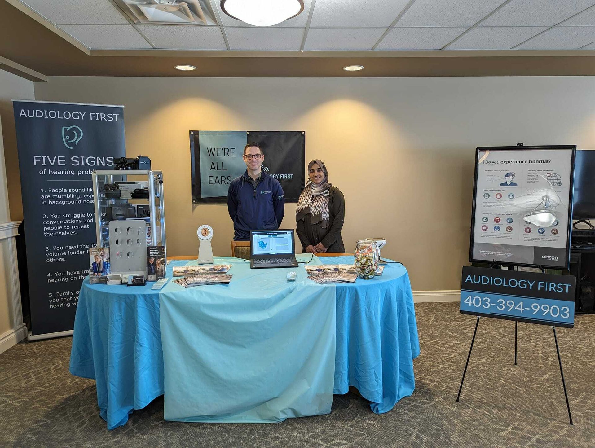 Audiology First booth with hearing aids, brochures, and signage at an event.