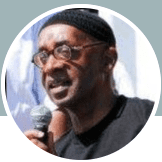 A man wearing glasses and a hat is holding a microphone.