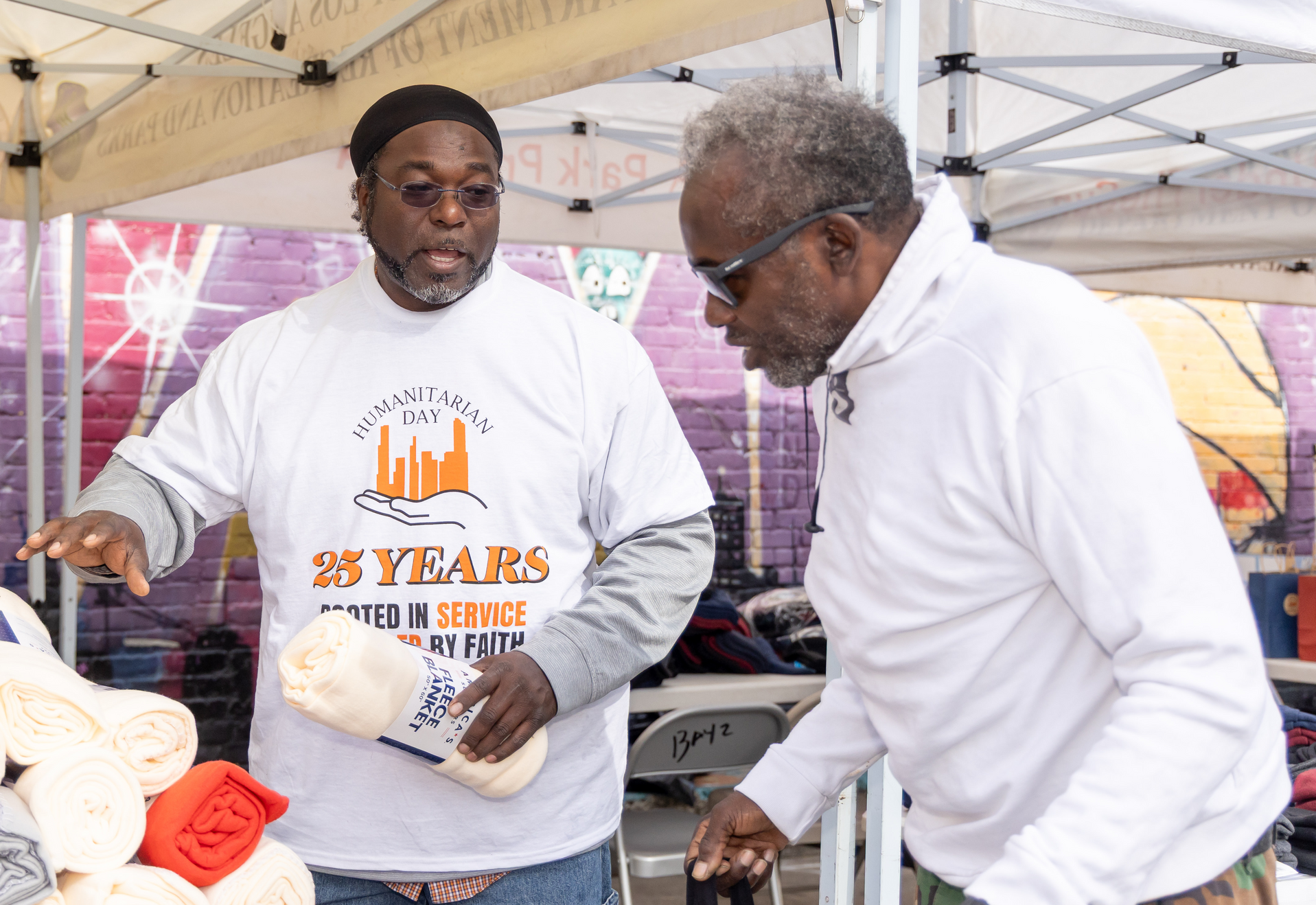 Two men are standing under a tent and one of them is wearing a shirt that says 25 years