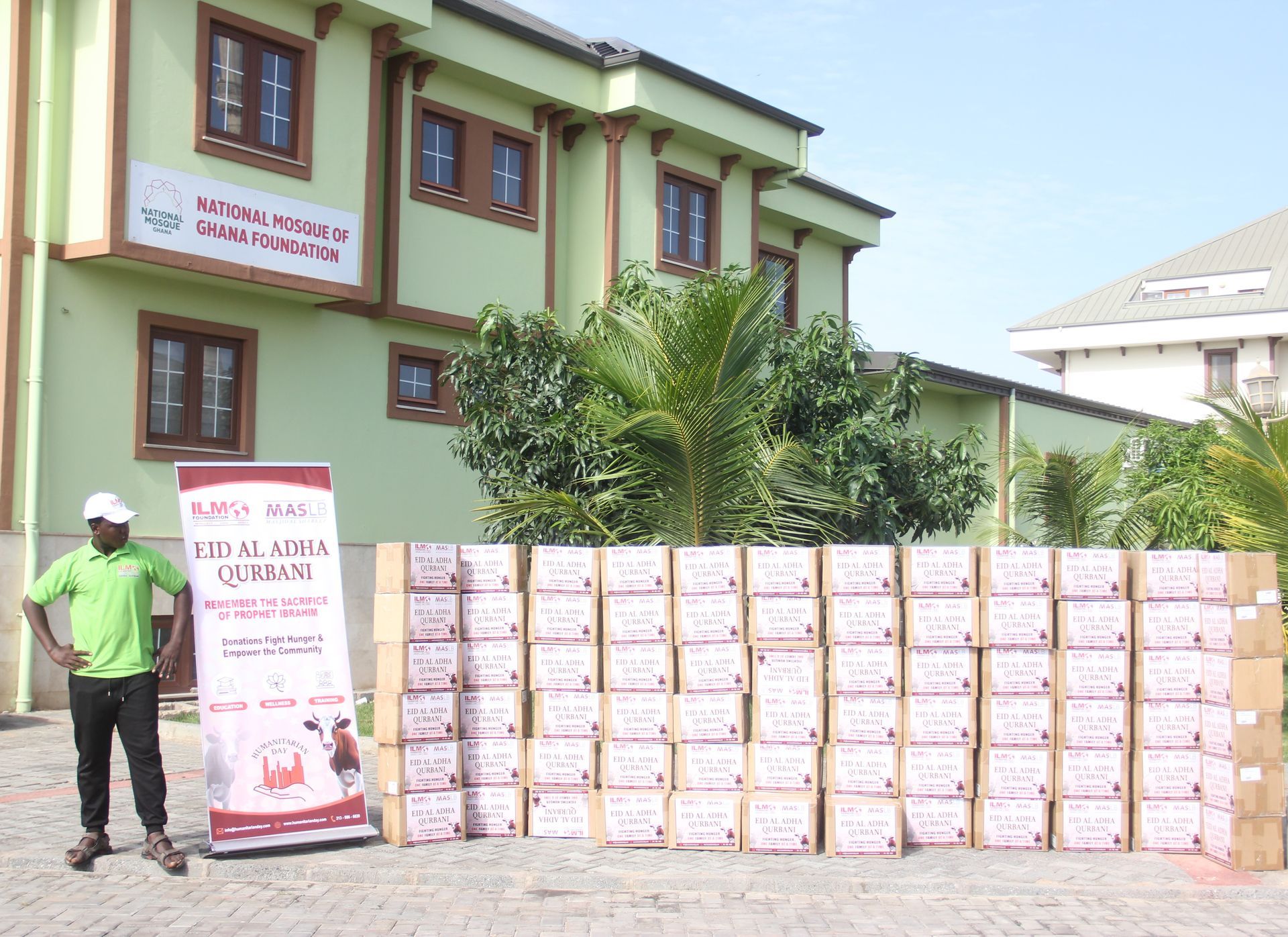 A man in a green shirt stands in front of a building with boxes in front of it
