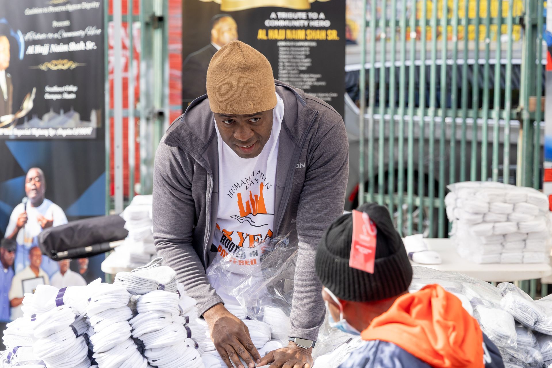 A man is standing in front of a pile of clothes and talking to another man.