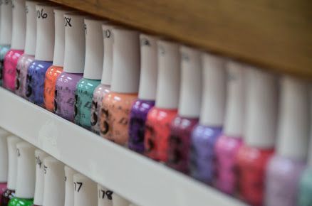 A row of bottles of nail polish are lined up on a shelf.