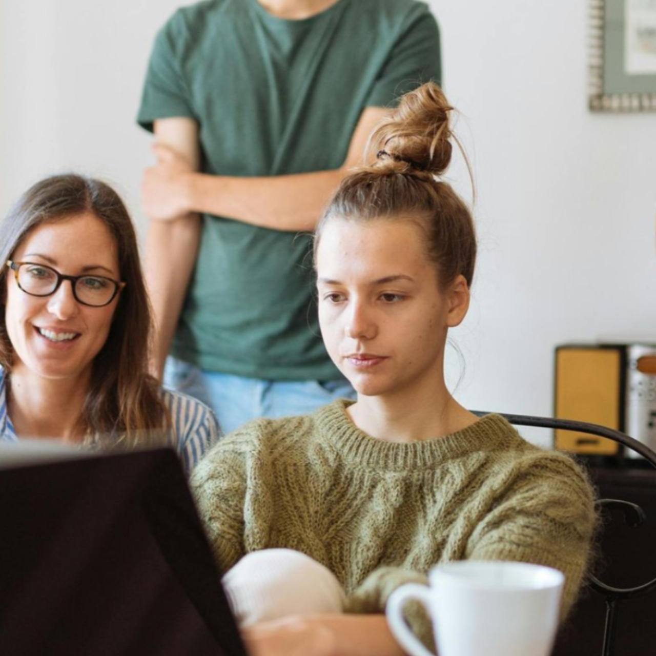 Three people looking at a laptop in a well-lit room. Two women and a man, possibly collaborating.