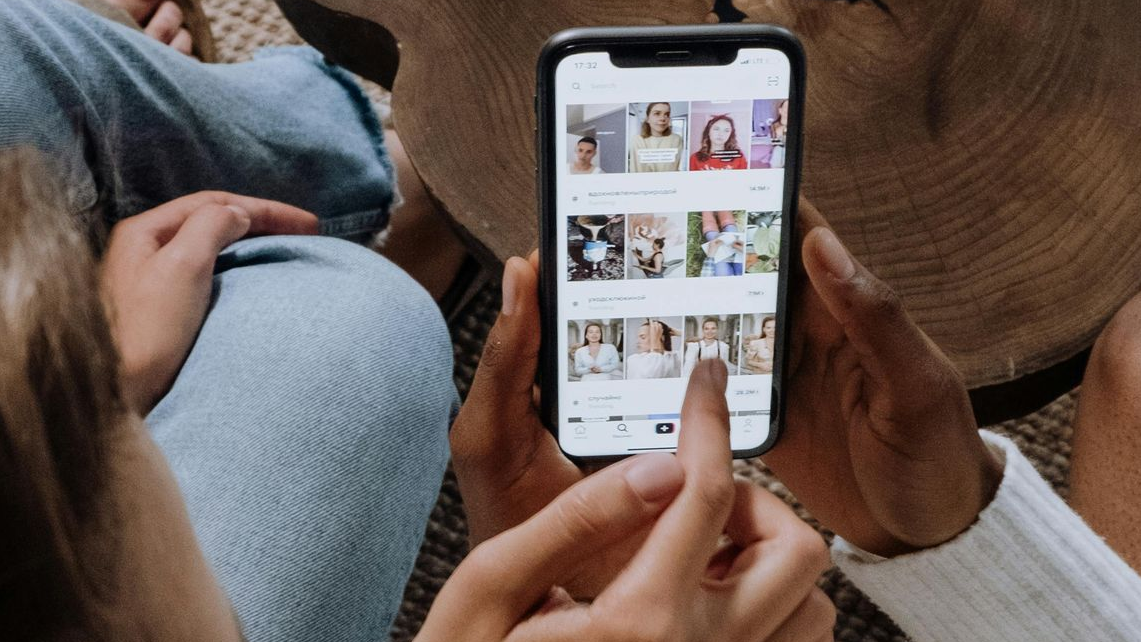 Hands holding a phone, scrolling through images. A person's legs are visible in the background.