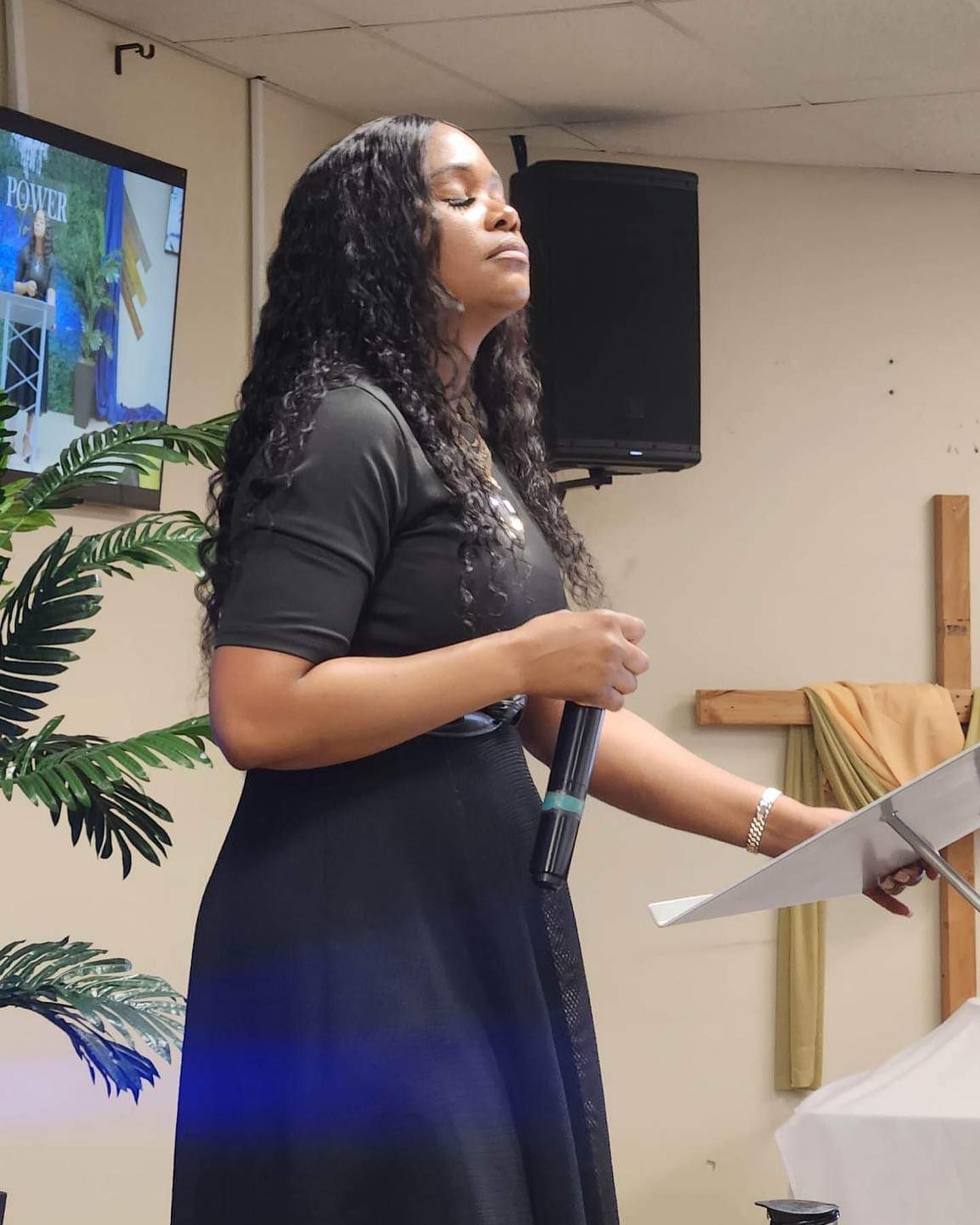 A woman in a black dress is preaching into a microphone
