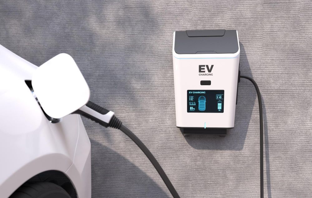 White electric vehicle charging at a wall-mounted EV charger. The charger has a small display screen.