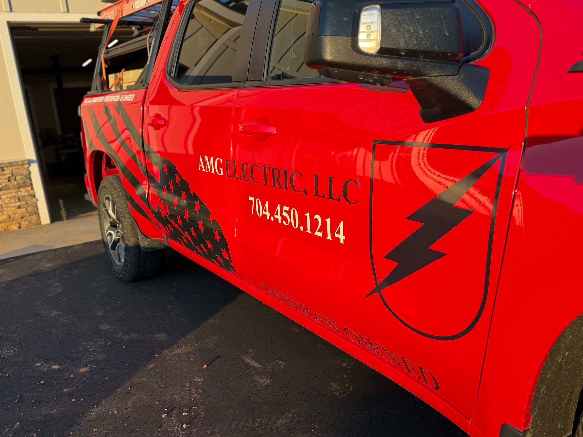 Electrician in hard hat and safety glasses using a tablet, inspecting electrical panel.