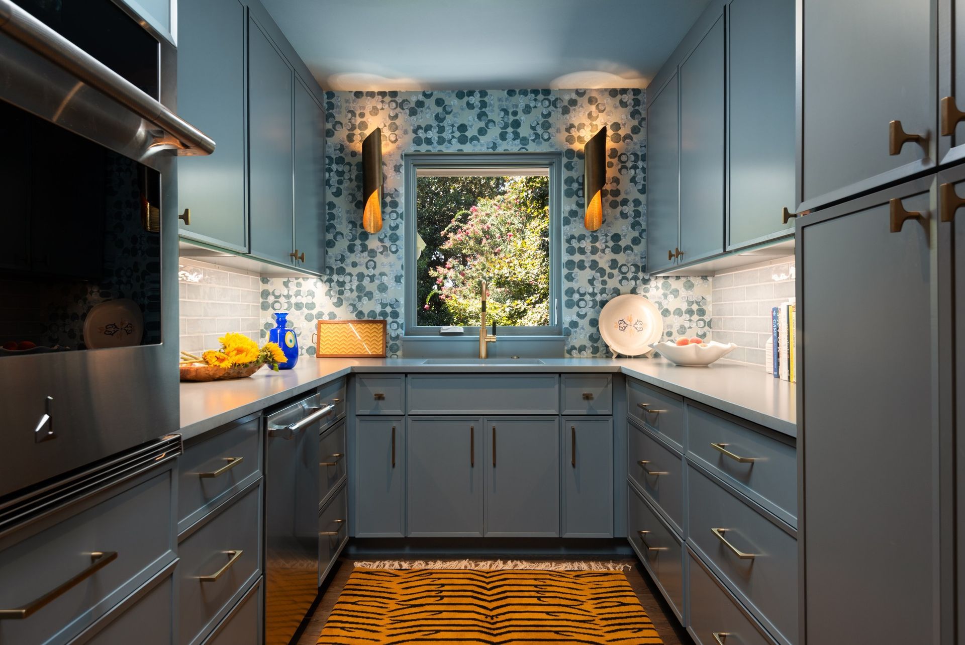 Man in a hard hat on a scaffold installs electrical wiring on a white ceiling; a brick wall and window are in the background.
