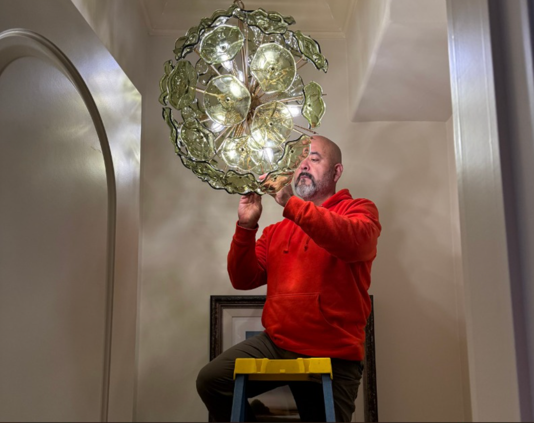 Electrician working on electrical panel, wearing a hard hat and tool belt.