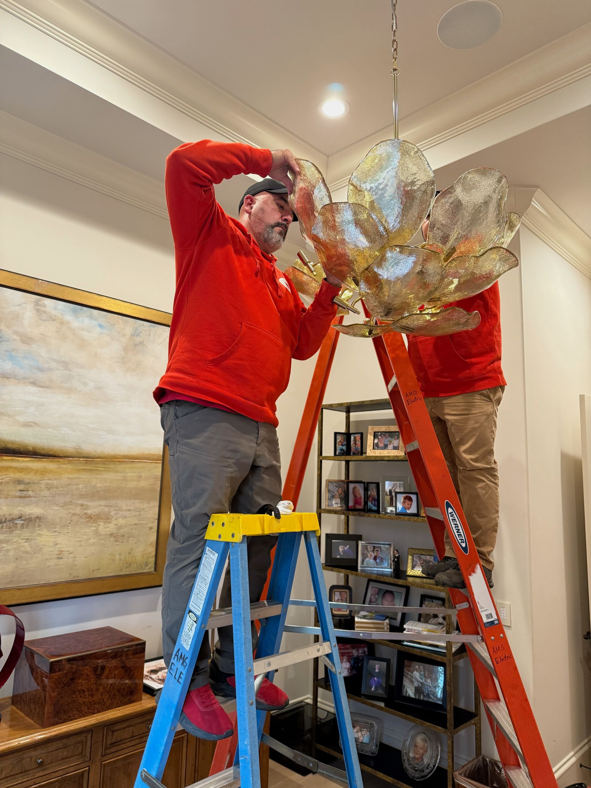 Electrician in hard hat, gloves, working on electrical panel, holding wires.