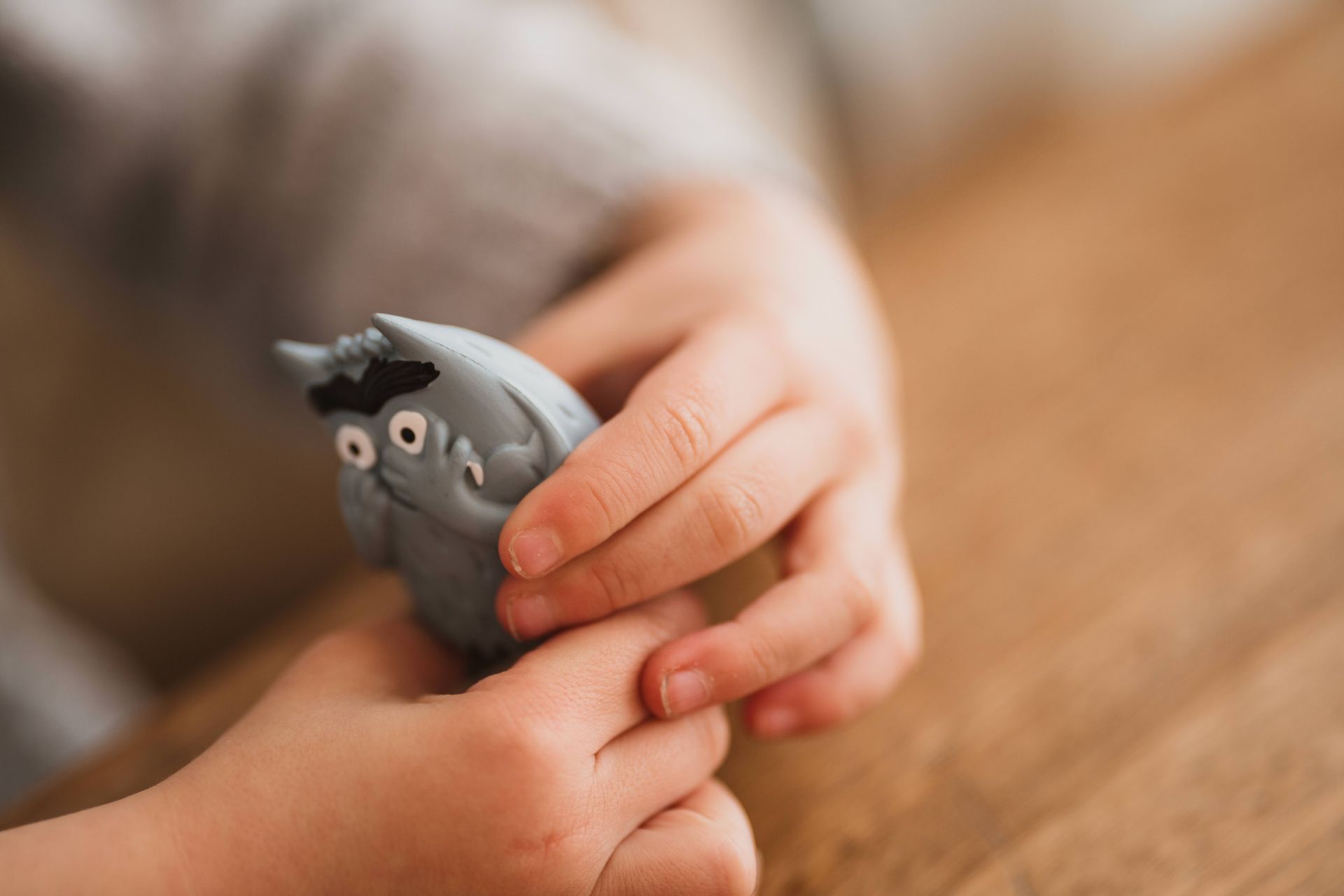 Mains d'enfant tenant un jouet hibou gris de dessin animé sur une surface en bois.