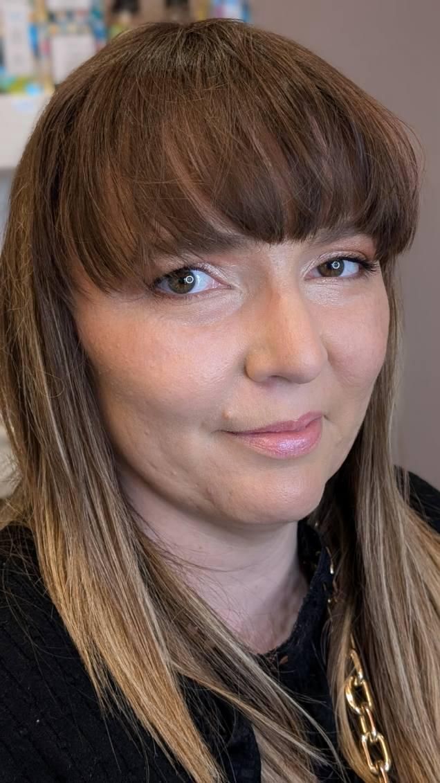 Femme à la peau claire, aux cheveux bruns avec une frange et une chaîne en or, souriante.