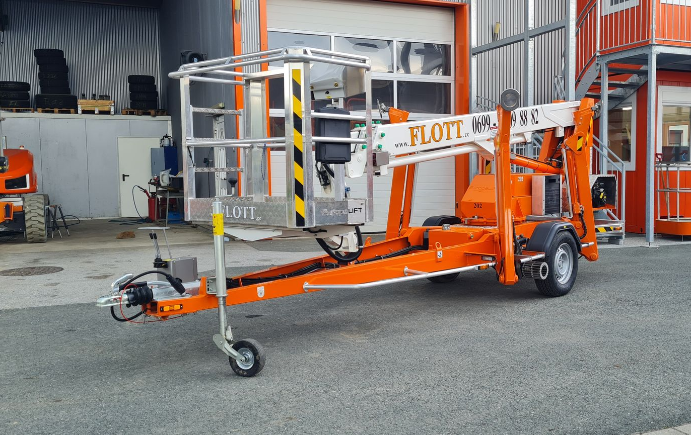 Orangefarbene, auf einem Anhänger montierte Hebebühne mit erhöhter Plattform, im Freien geparkt.