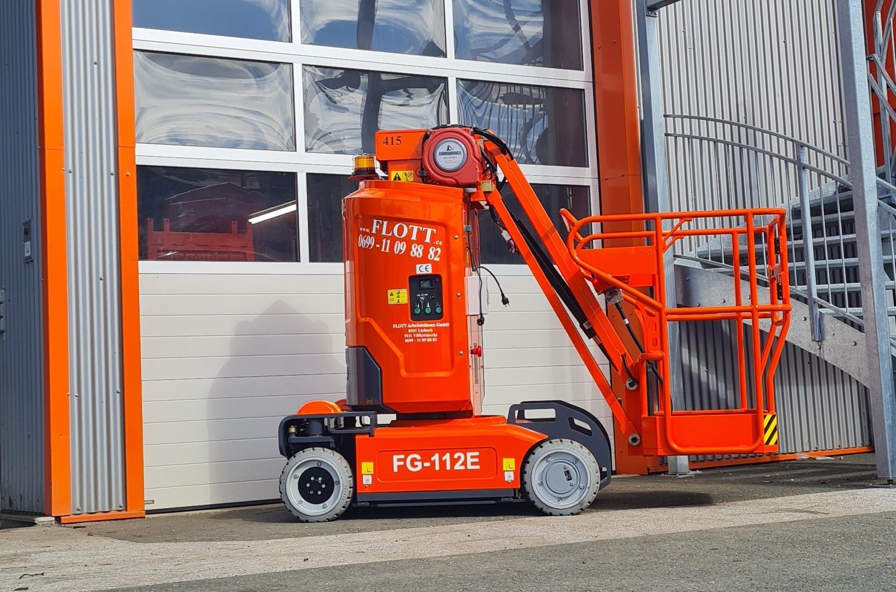 Eine orangefarbene JLG-Hubarbeitsbühne, Modell FG-112E, steht vor einem Gebäude.