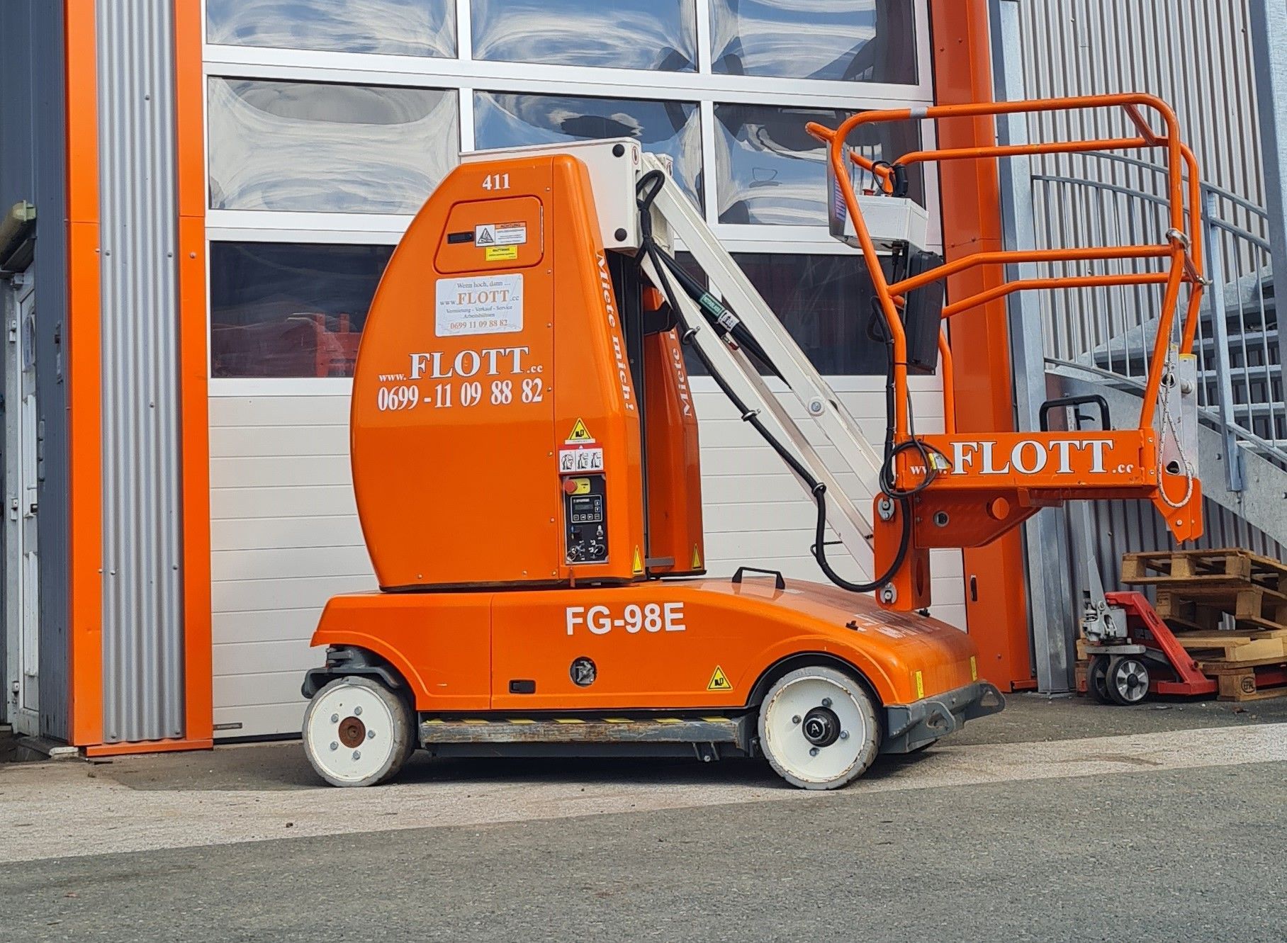 Orangefarbene Flott FG-98E Hubarbeitsbühne vor einem Gebäude mit weißem Garagentor.