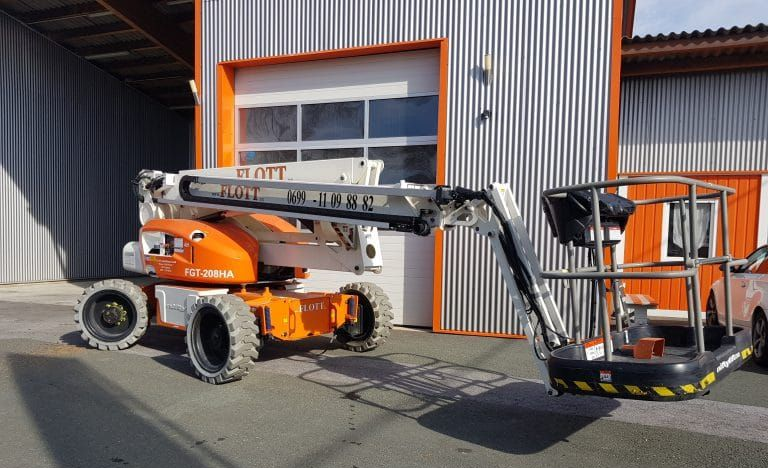 Eine orange-weiße Hubarbeitsbühne steht vor einem Gebäude mit Wellblechfassade.