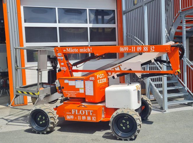 Eine orangefarbene Hubarbeitsbühne der Marke „FLOTT“ parkt vor einem Gebäude mit weißer Tür.