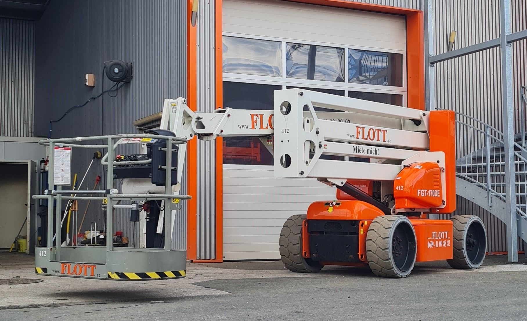 Orange-weiße Hubarbeitsbühne vor einem Gebäude mit geschlossenem Garagentor.