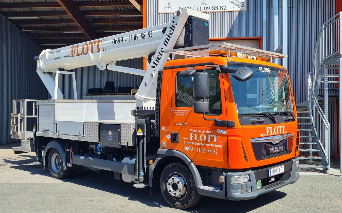 Ein orangefarbener MAN-Lkw mit ausgefahrener Hubarbeitsbühne steht in der Nähe eines Gebäudes mit Treppe.