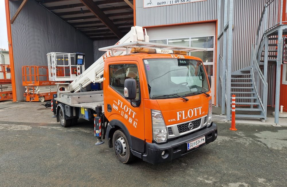 Oranger Nissan-Lkw mit Hubarbeitsbühne; vor dem Gebäude geparkt. „FLOTT“-Logo an der Seite.