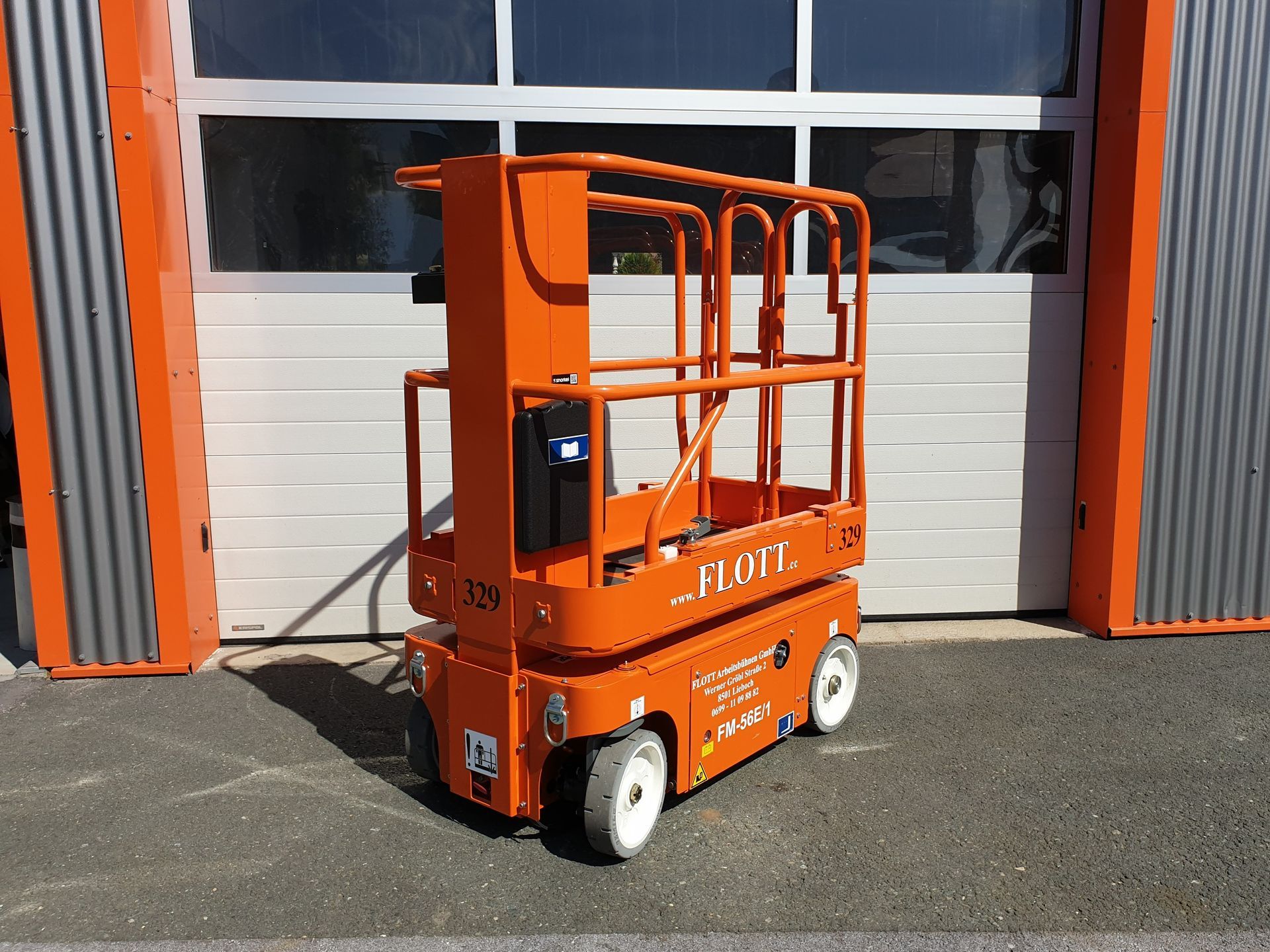 Eine orangefarbene, selbstfahrende Hubarbeitsbühne vor einem weißen Garagentor.