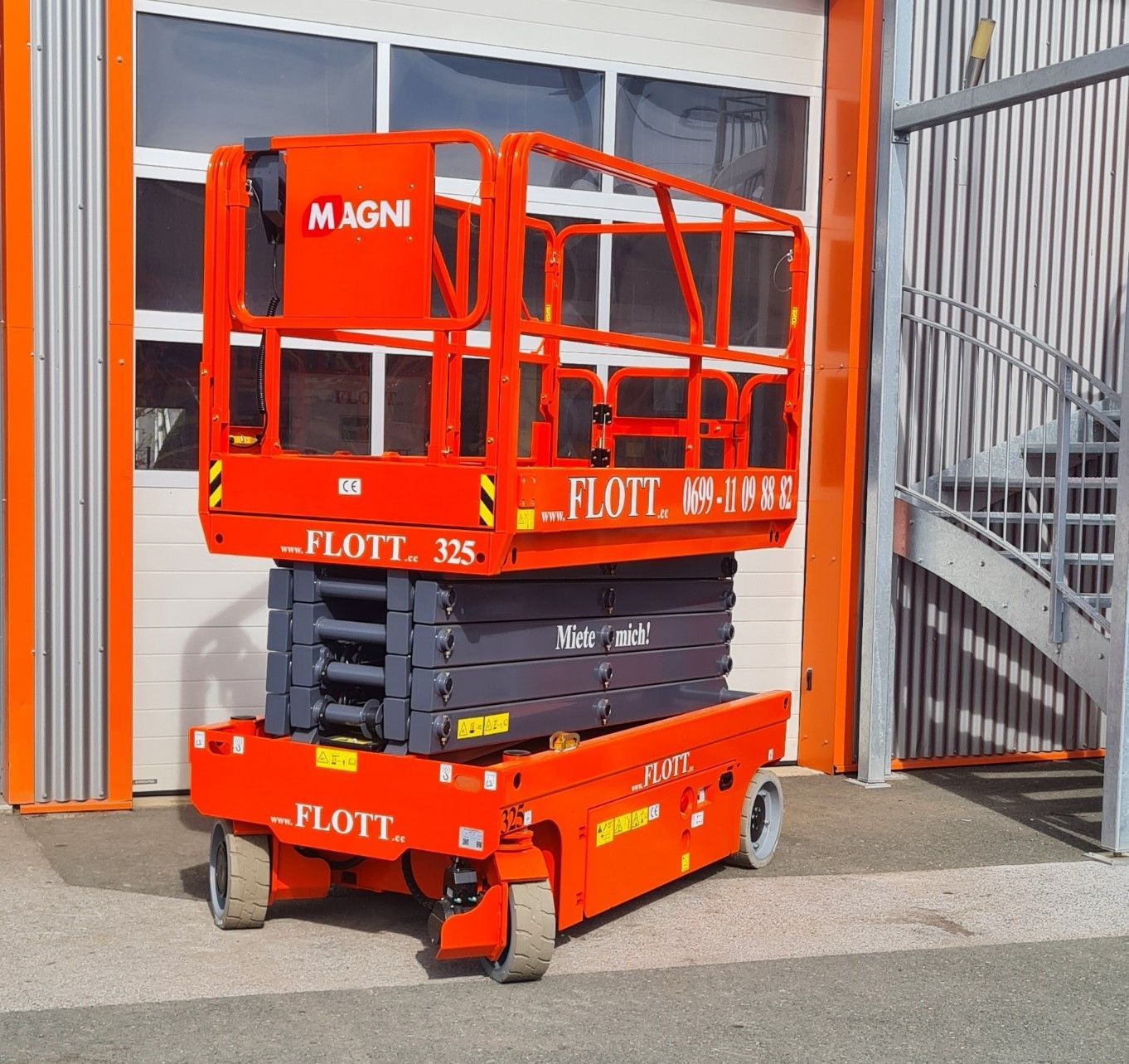 Orangefarbene Scherenhebebühne der Marke „MAGNI“ vor einem Gebäude.