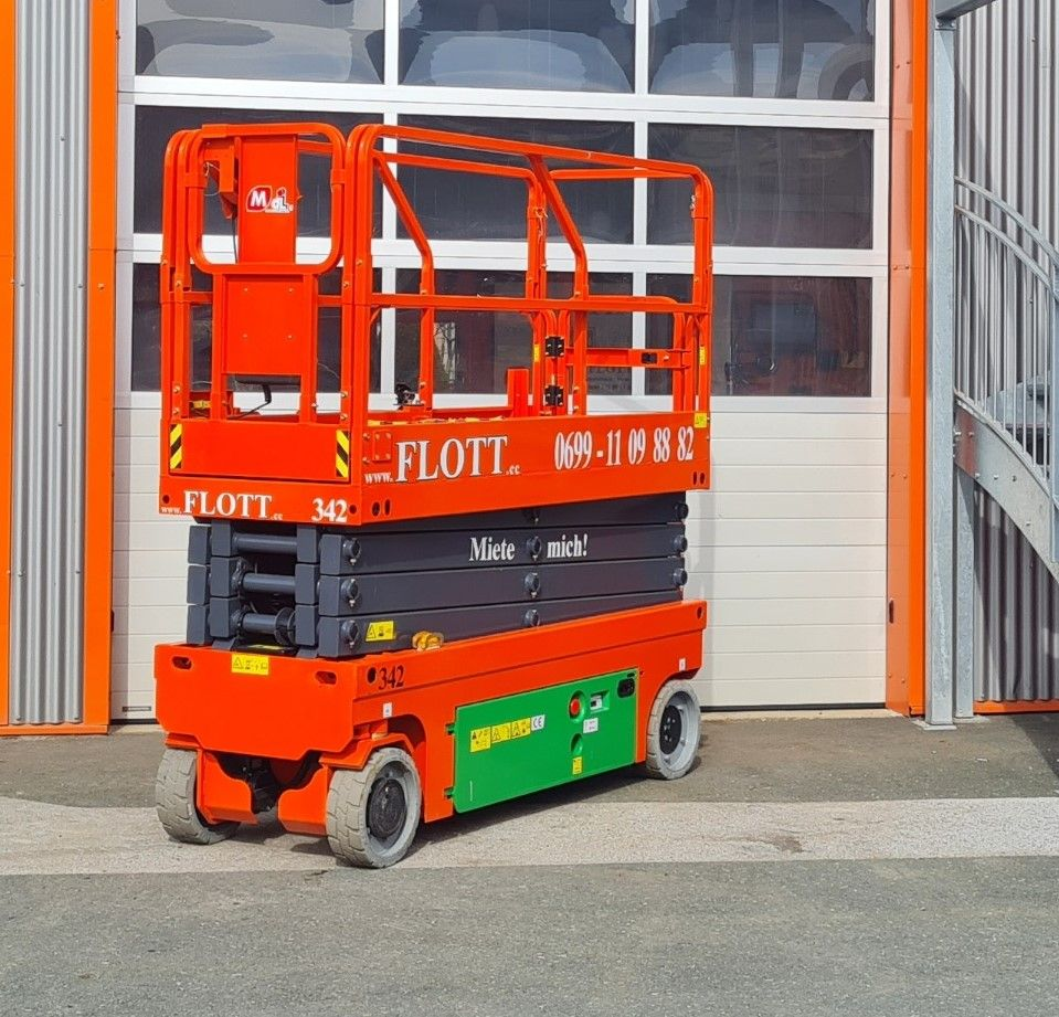 Eine orange-grüne Scherenhebebühne vor einem weißen Garagentor.