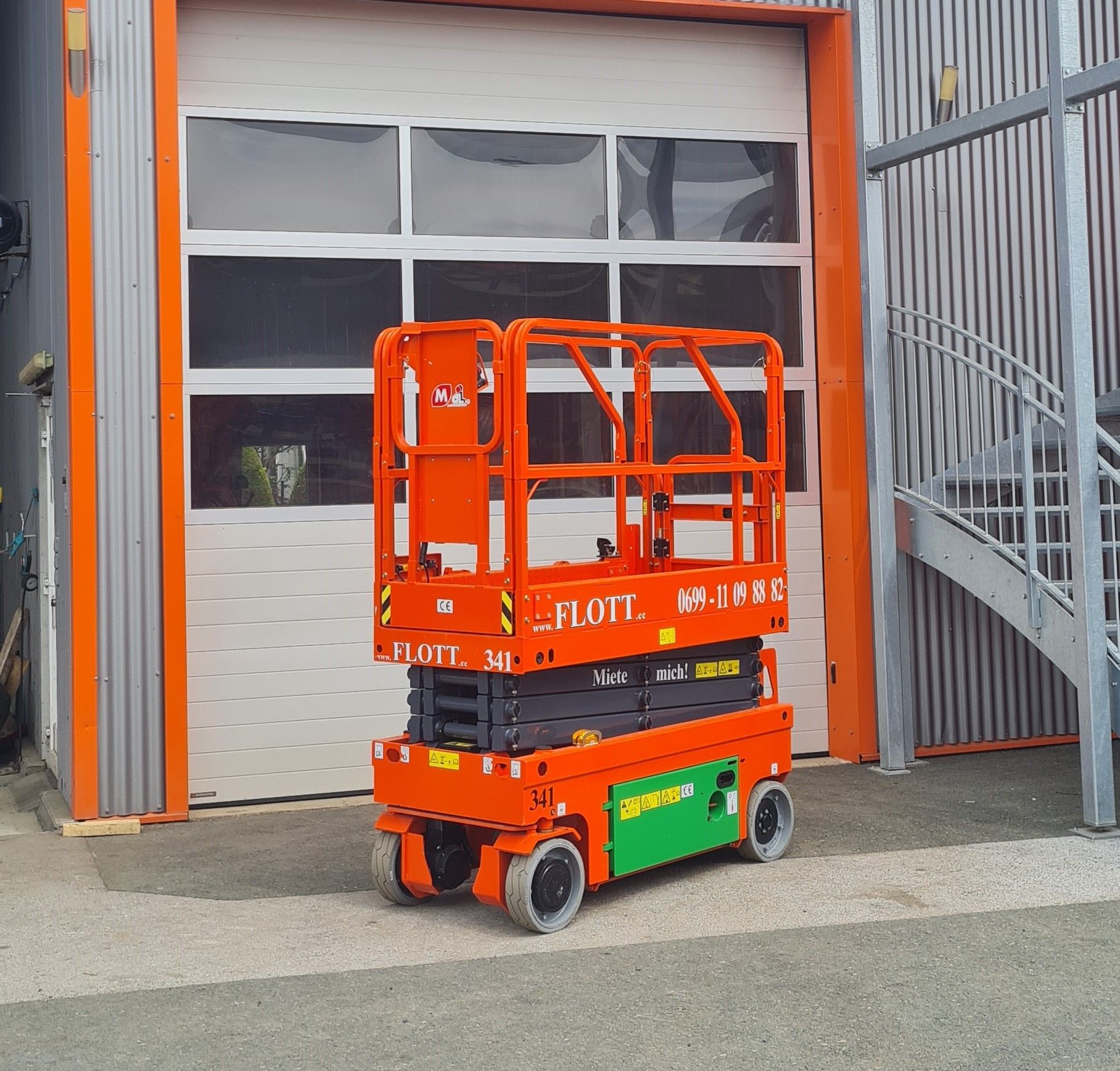Eine orangefarbene Scherenhebebühne vor einem weißen Garagentor.