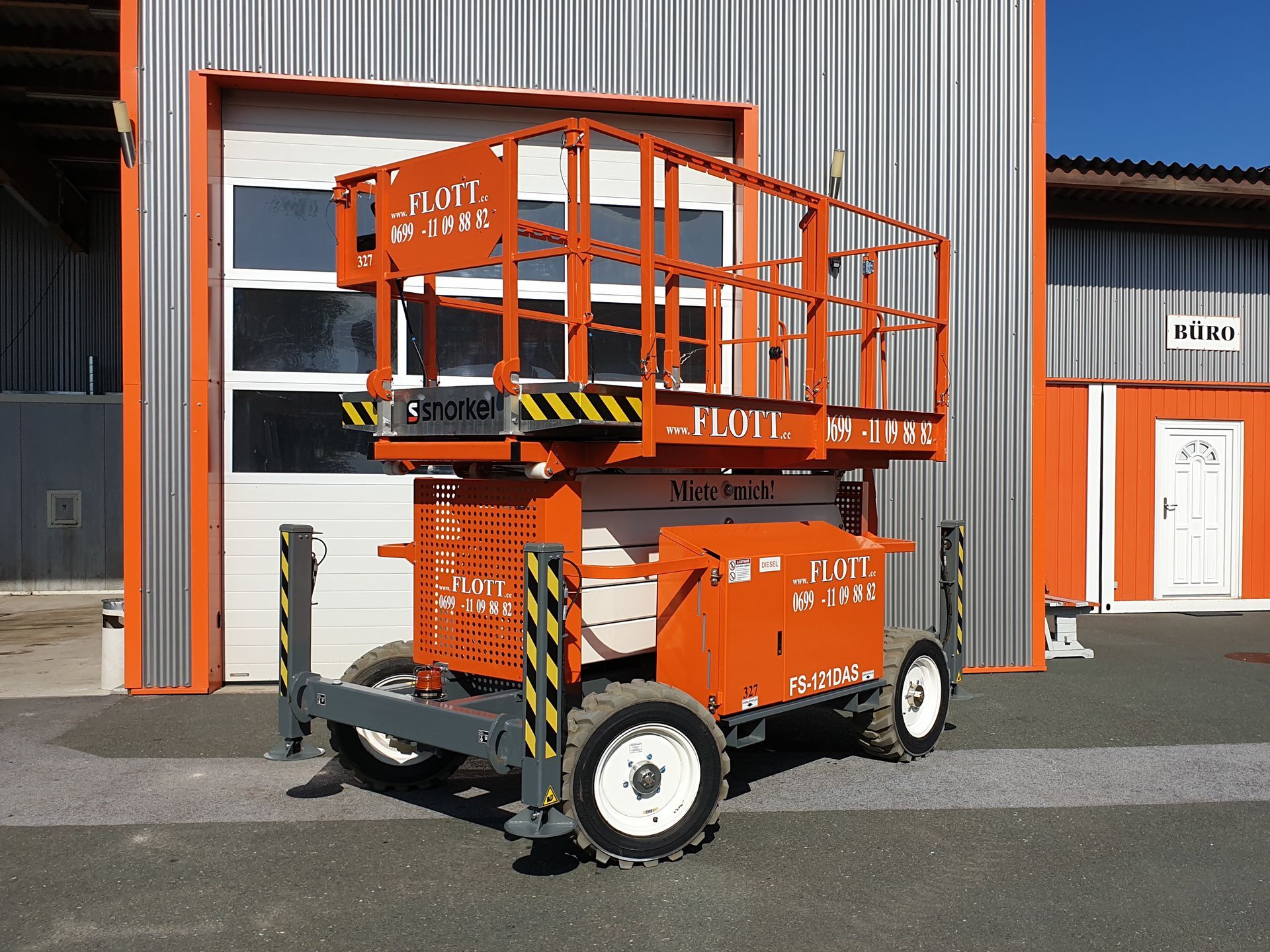 Eine orangefarbene mobile Hubarbeitsbühne steht vor einem Gebäude mit geschlossenem Garagentor.