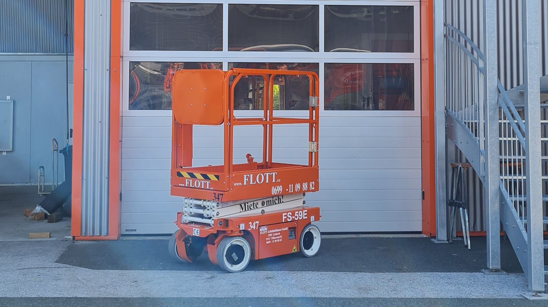 Eine orangefarbene Scherenhebebühne vor einem geschlossenen Garagentor.