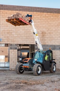 Ein Teleskoplader hebt eine Palette mit Pflastersteinen auf einer Baustelle an.