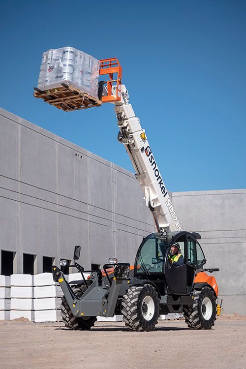 Auf einer Baustelle hebt ein Teleskoplader eine Palette mit verpackten Waren an.