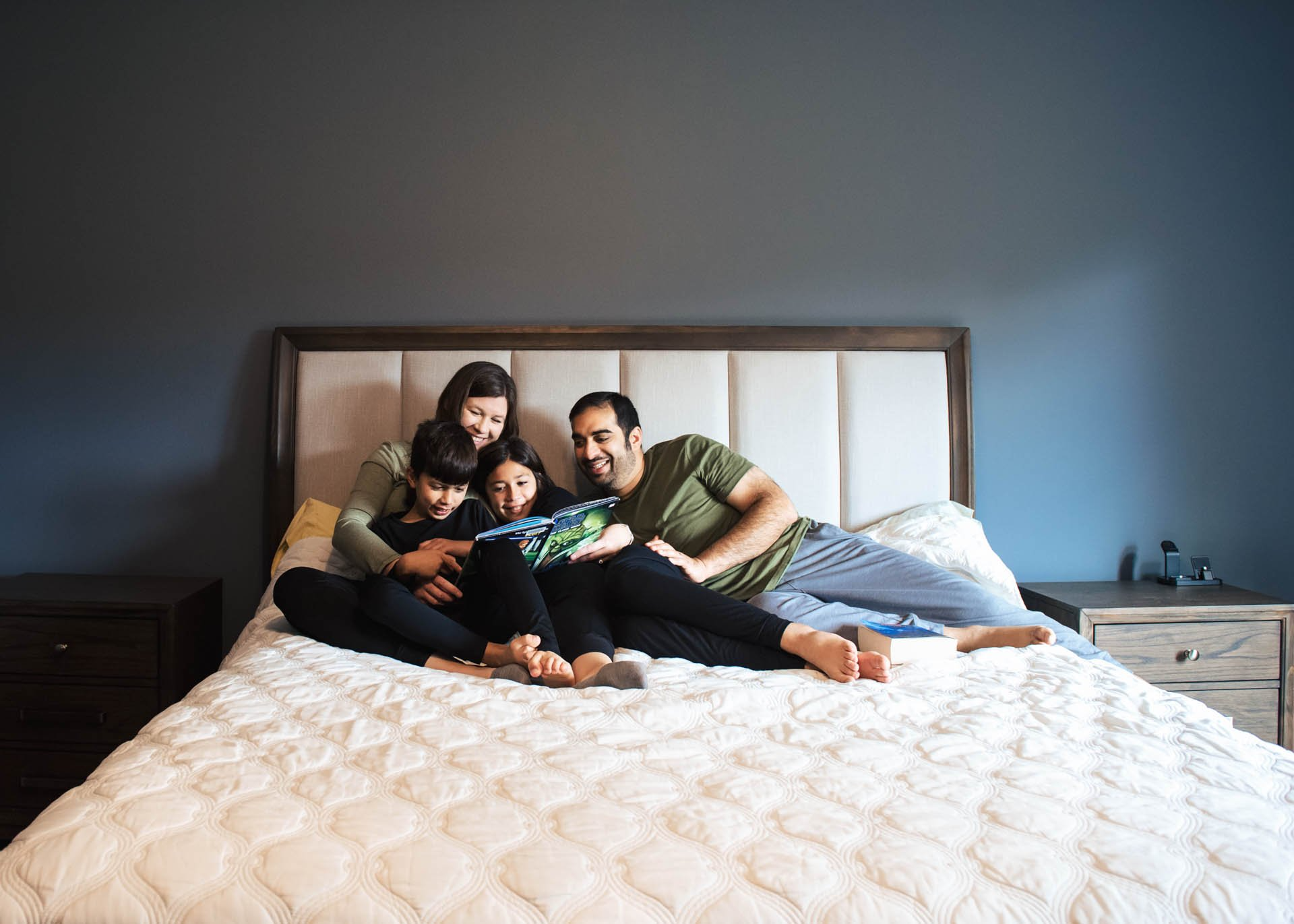 A family is sitting on a bed looking at a tablet.