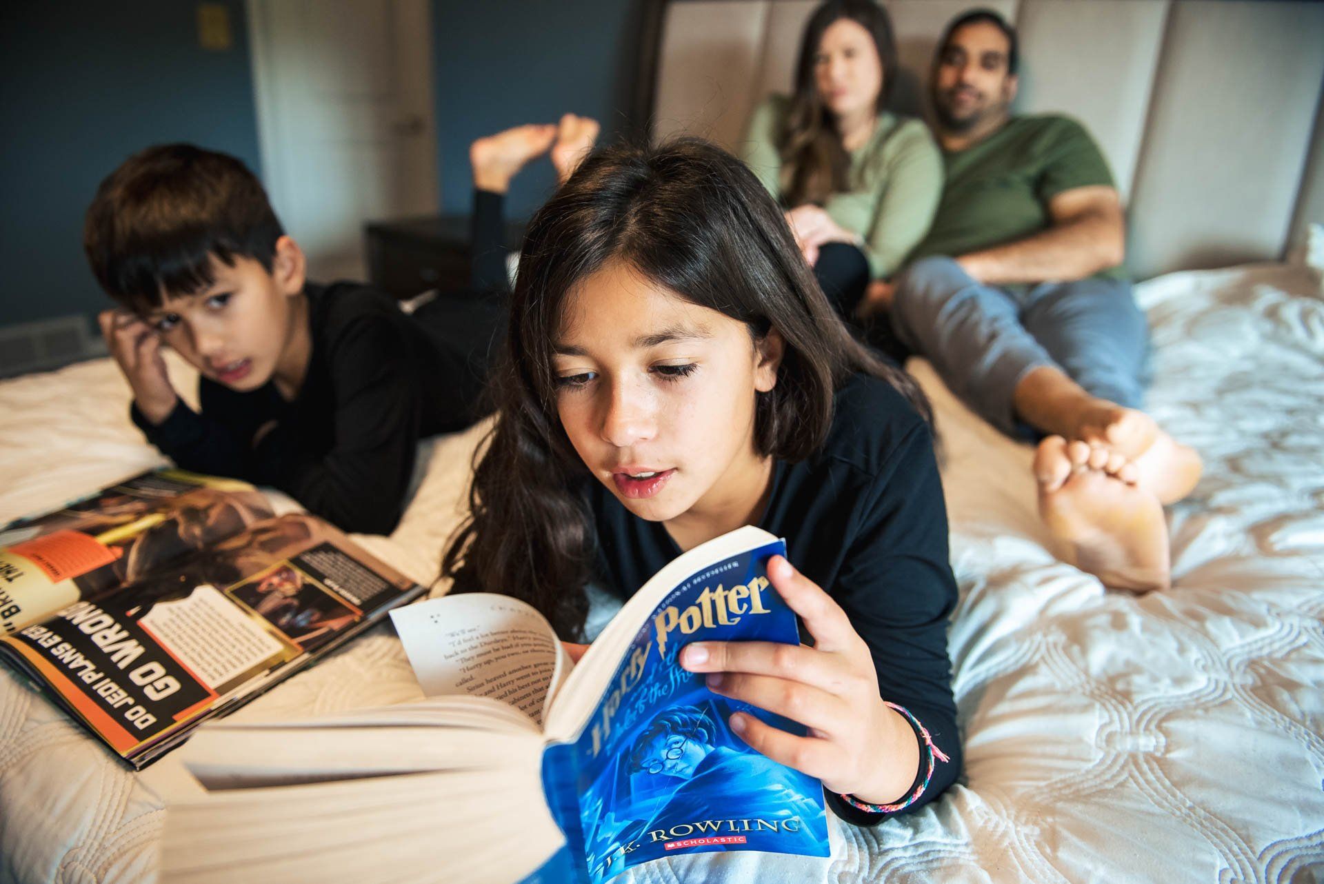 A family is laying on a bed reading harry potter books.