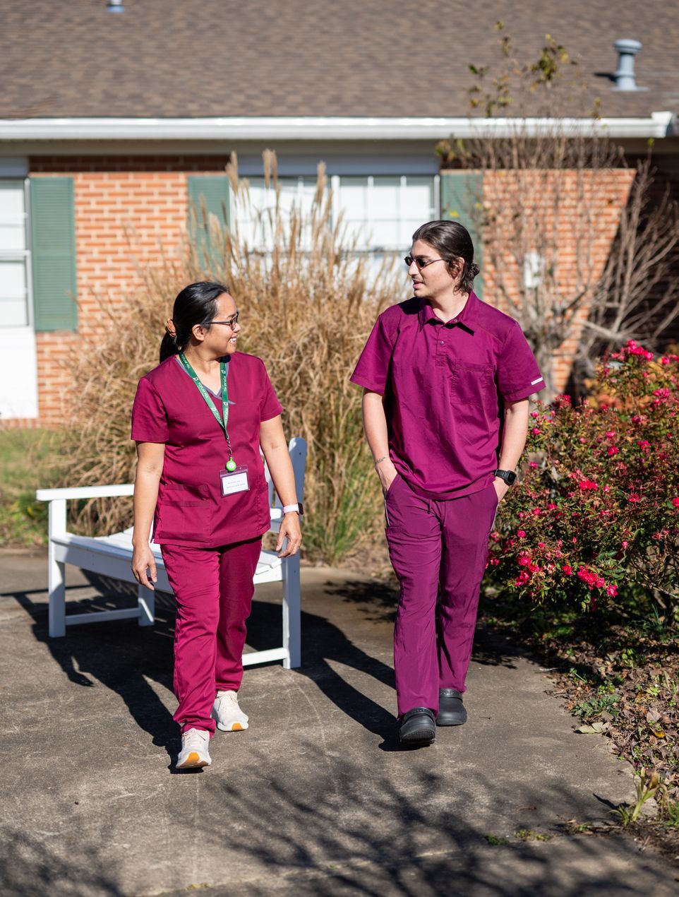 Two nurses are walking down a sidewalk in front of the Poplar Hill