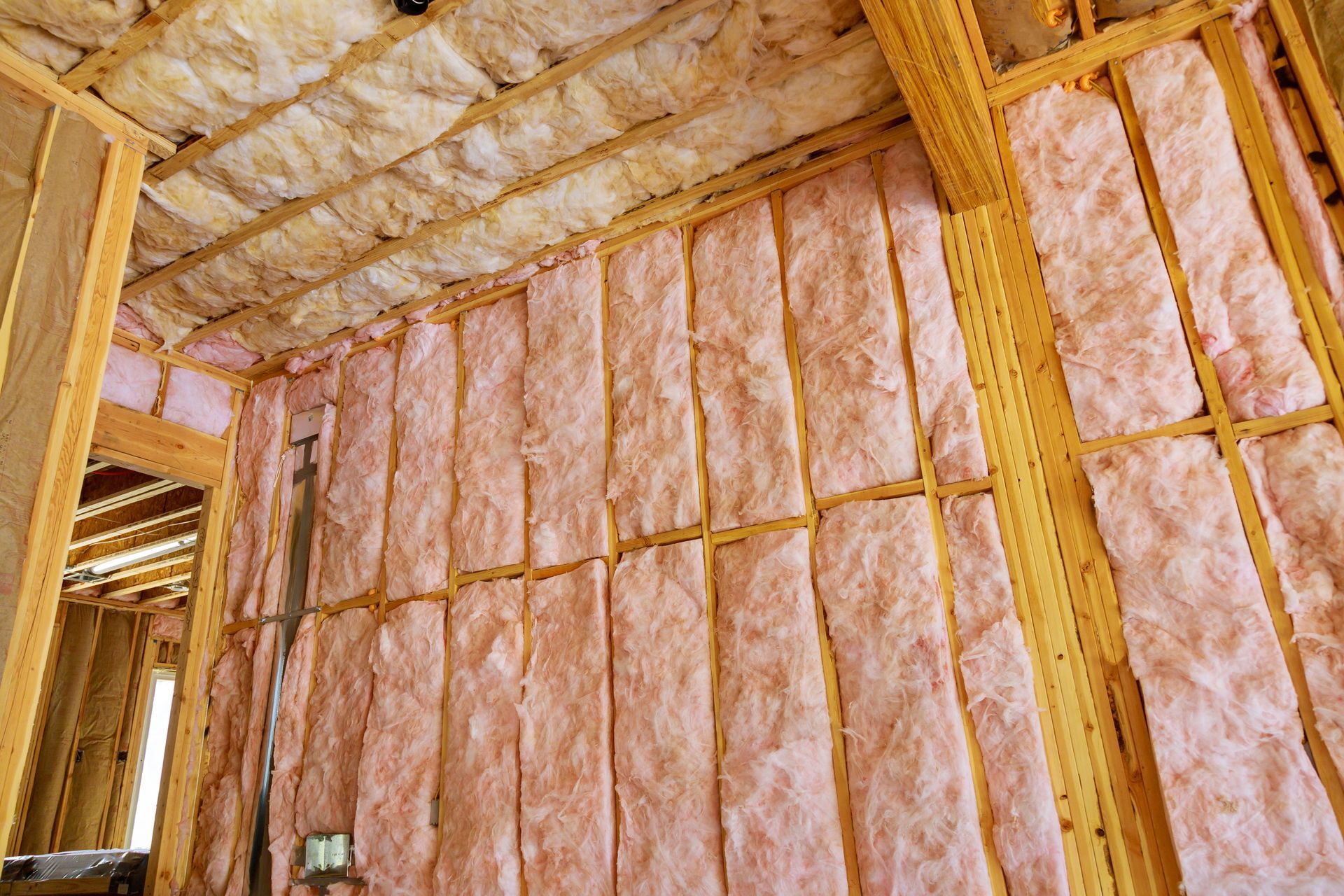 interior wall and ceiling framing with pink fiberglass insulation installed between wooden studs.
