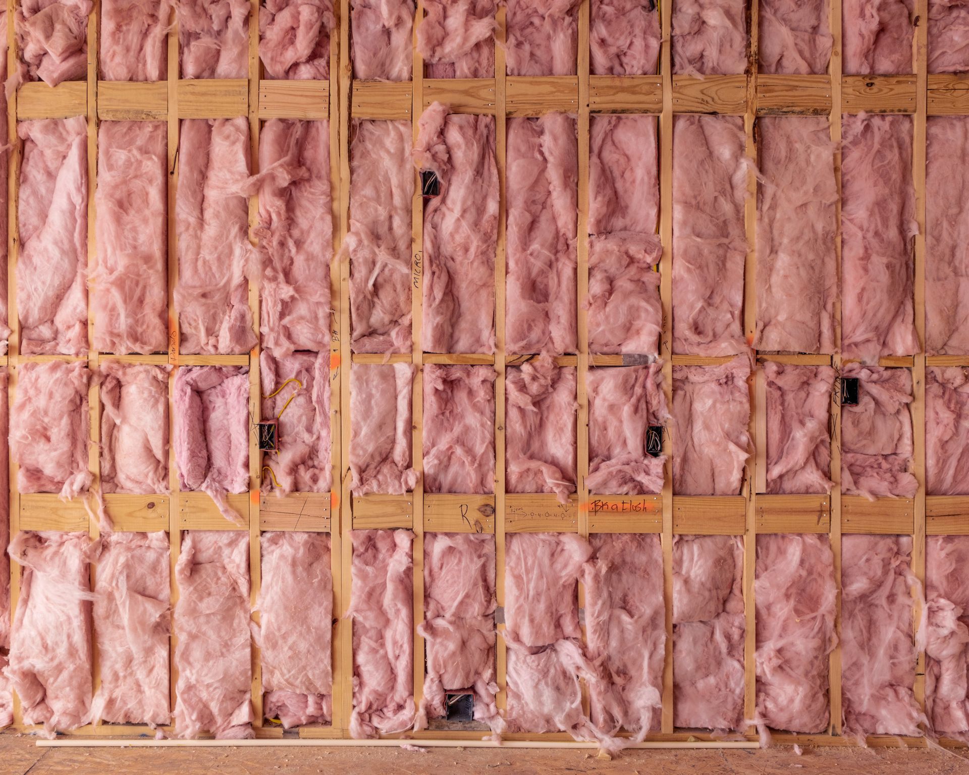 A pink fiberglass insulation installed between wooden wall studs
