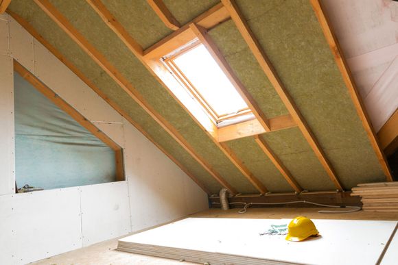 An attic with a skylight and a hard hat on the floor.