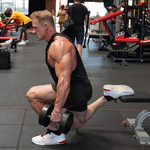 Ron Matthews  is squatting down while holding a dumbbell in a gym.