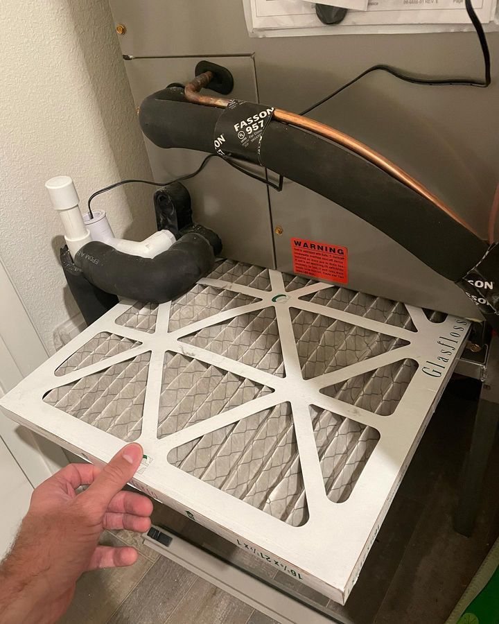 A person is pointing at a filter on top of a furnace.