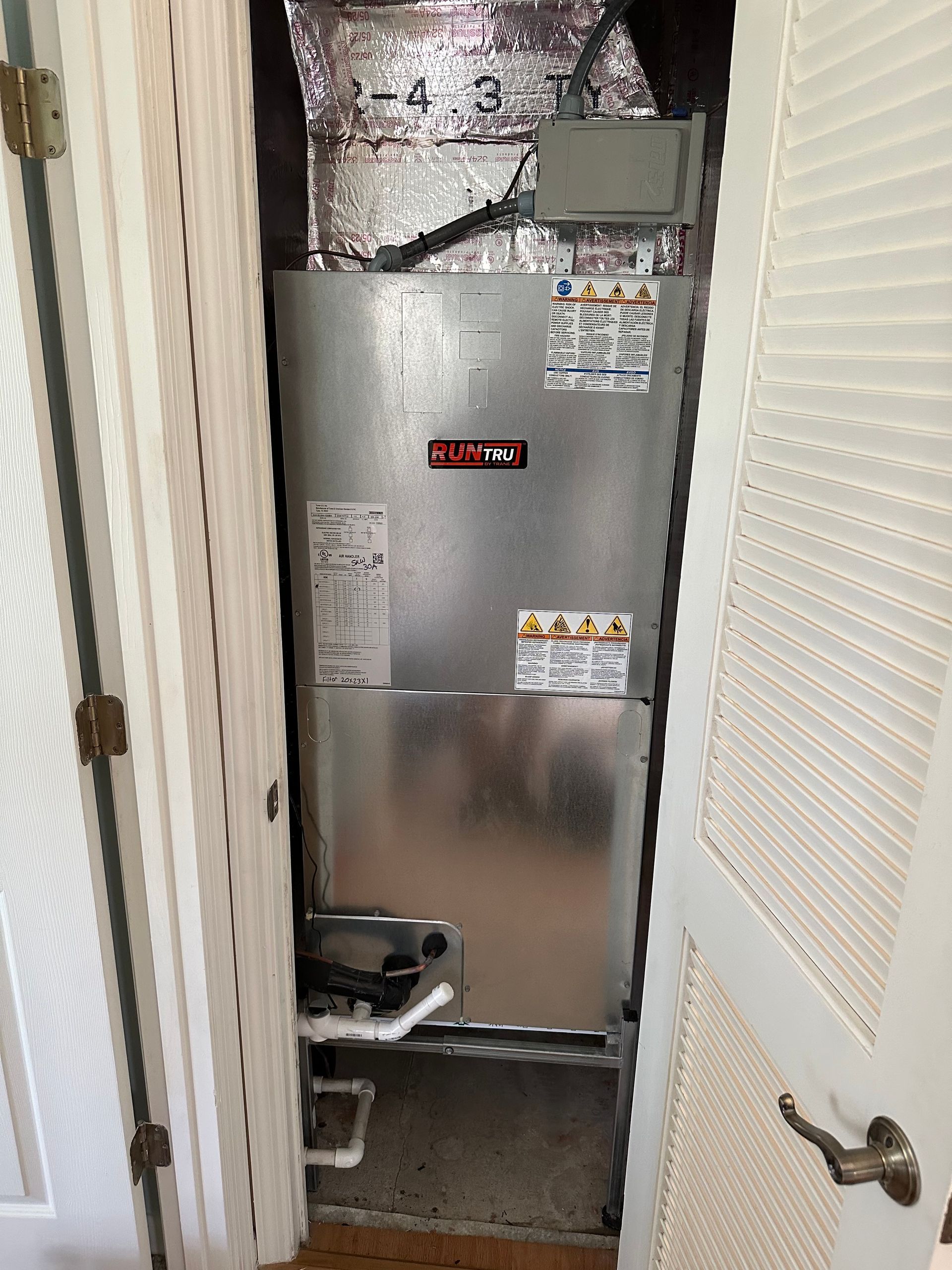 A furnace unit in a closet, surrounded by white doors and trim.