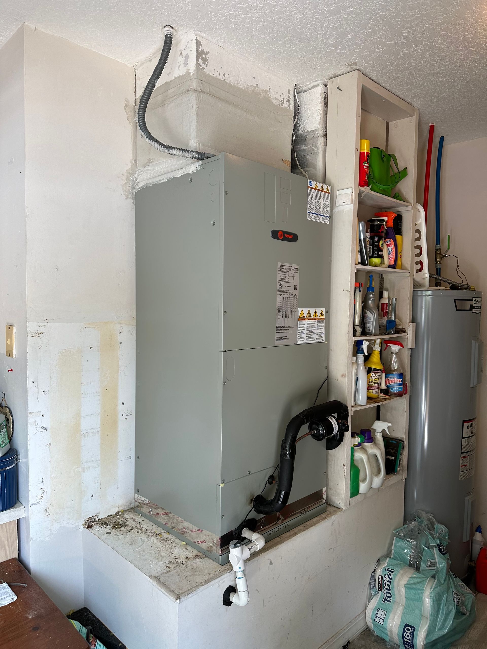 HVAC unit and water heater in a garage; gray metal, white shelves with cleaning supplies.