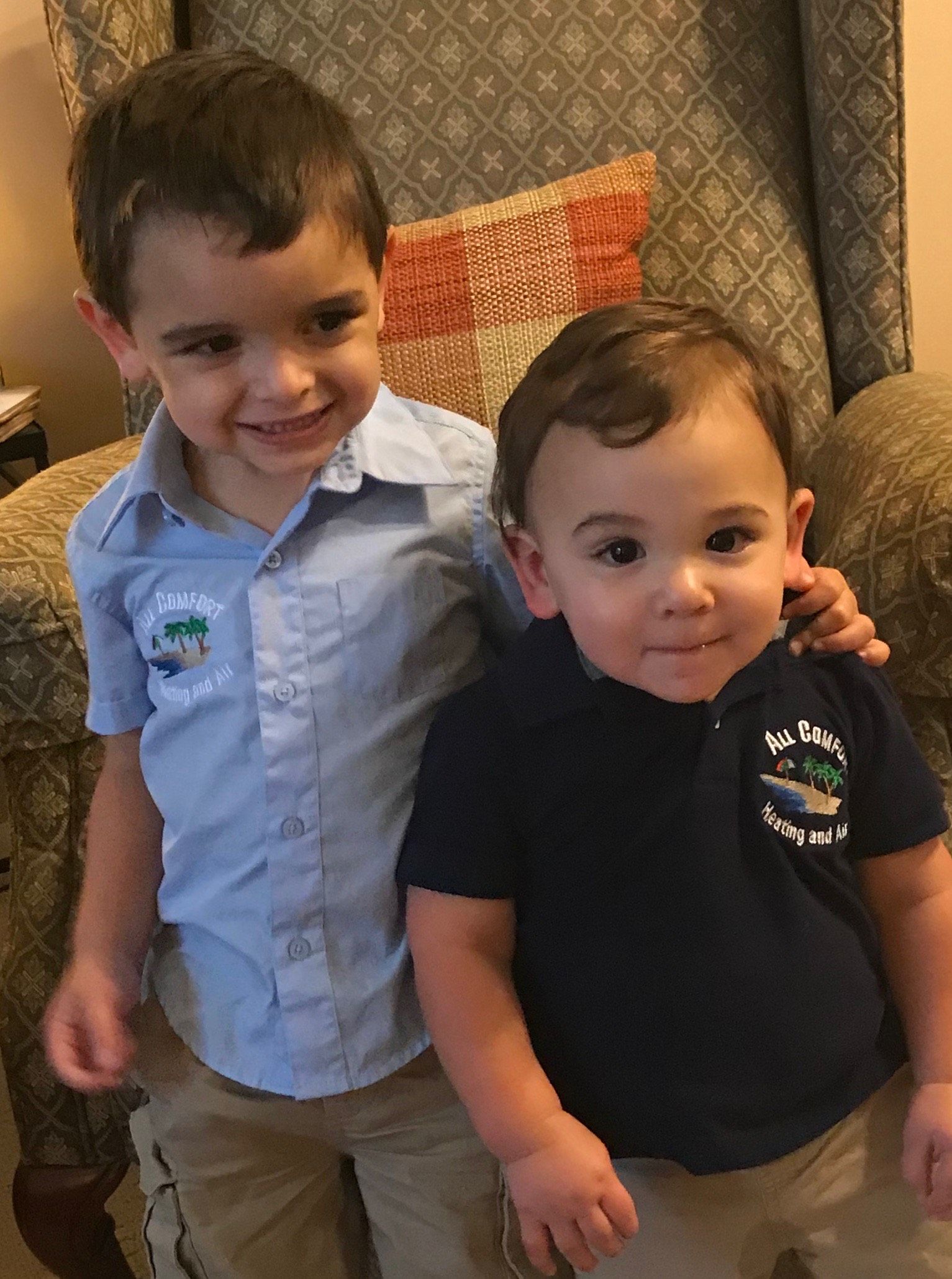 Two young boys smiling, one with an arm around the other, both wearing polo shirts.