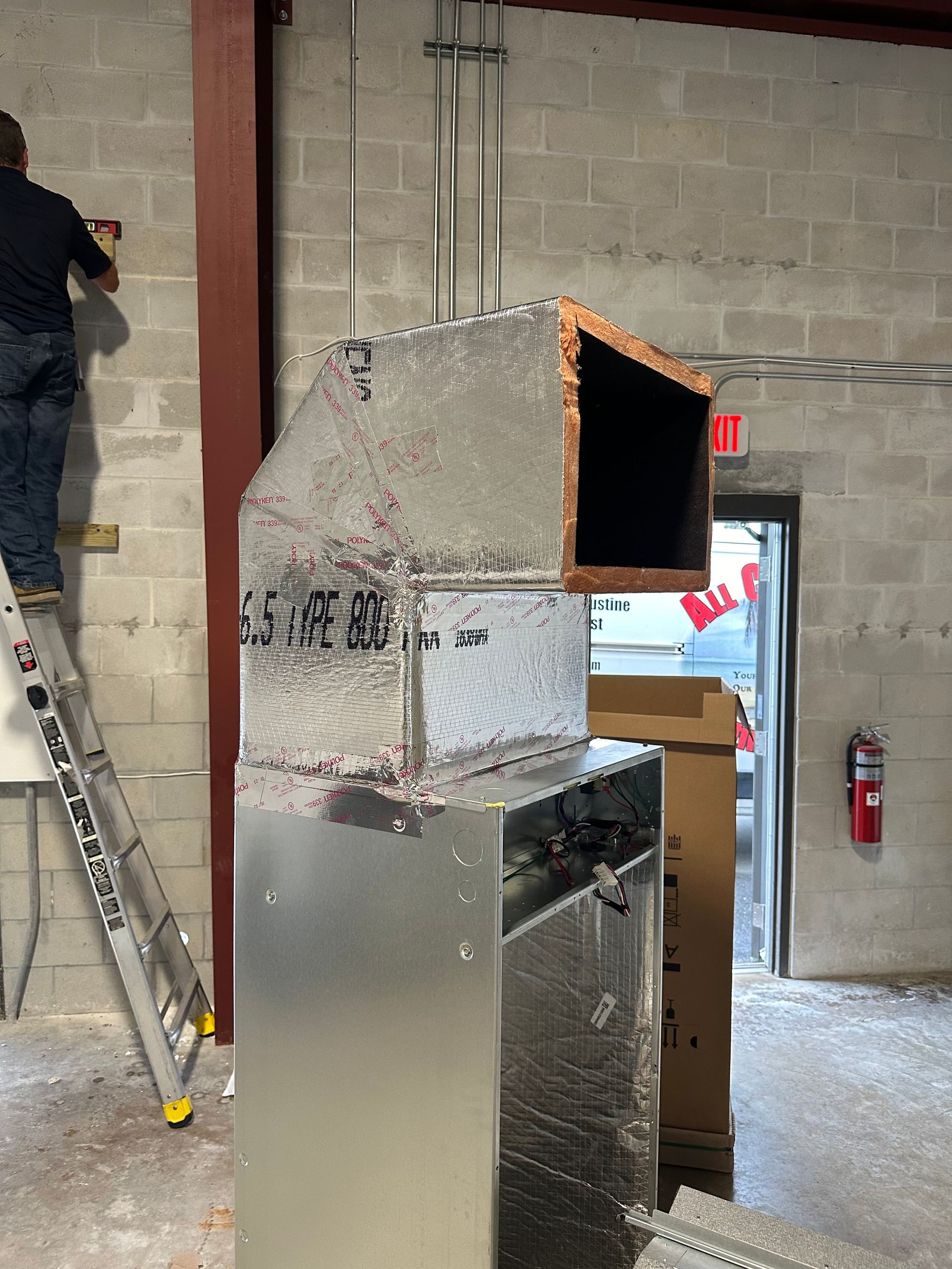 HVAC ductwork installation in a commercial space; worker on ladder.