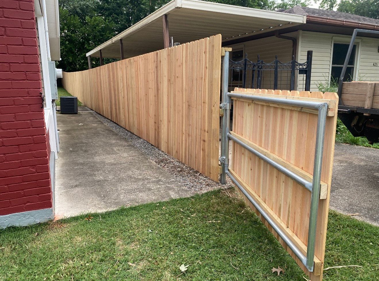 A weathered wooden fence adjoins a brick wall, with a gate slightly ajar, in a grassy yard.
